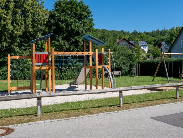 Kletterturm mit Hängebrücke und Rutsche, im Hintergrund Sitzbank und Schaukel